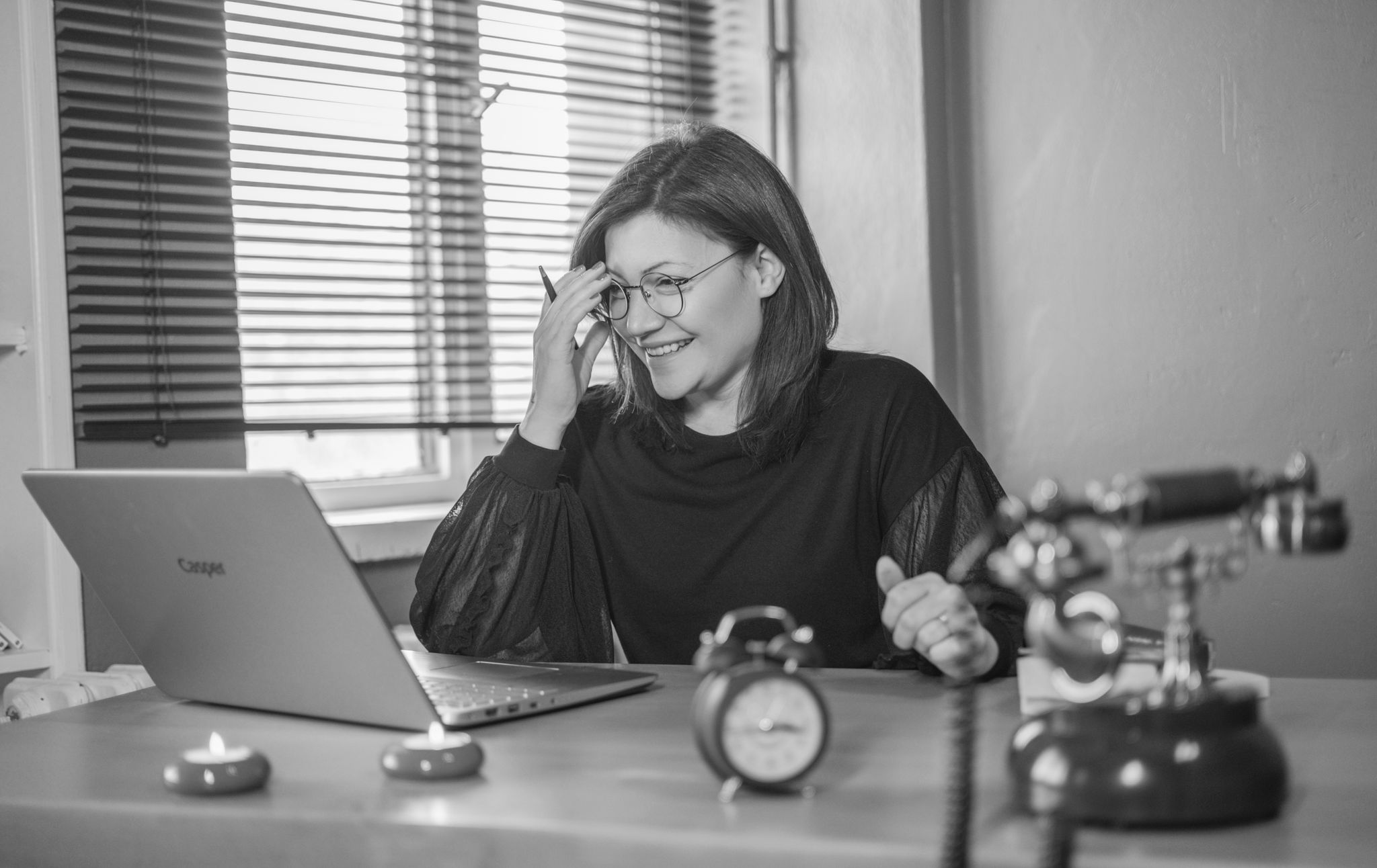 Services A businesswoman smiles while working on a laptop with vintage decor in a monochrome office.